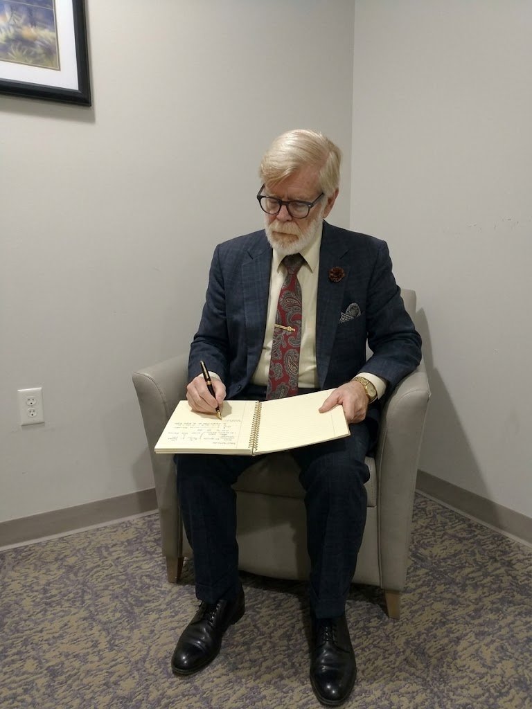 Gerald Wieczorek seated, writing in a field notebook